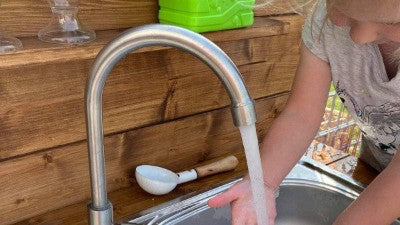 Kind spielt an Matschküche mit Wasserhahn im Garten und Kindergarten